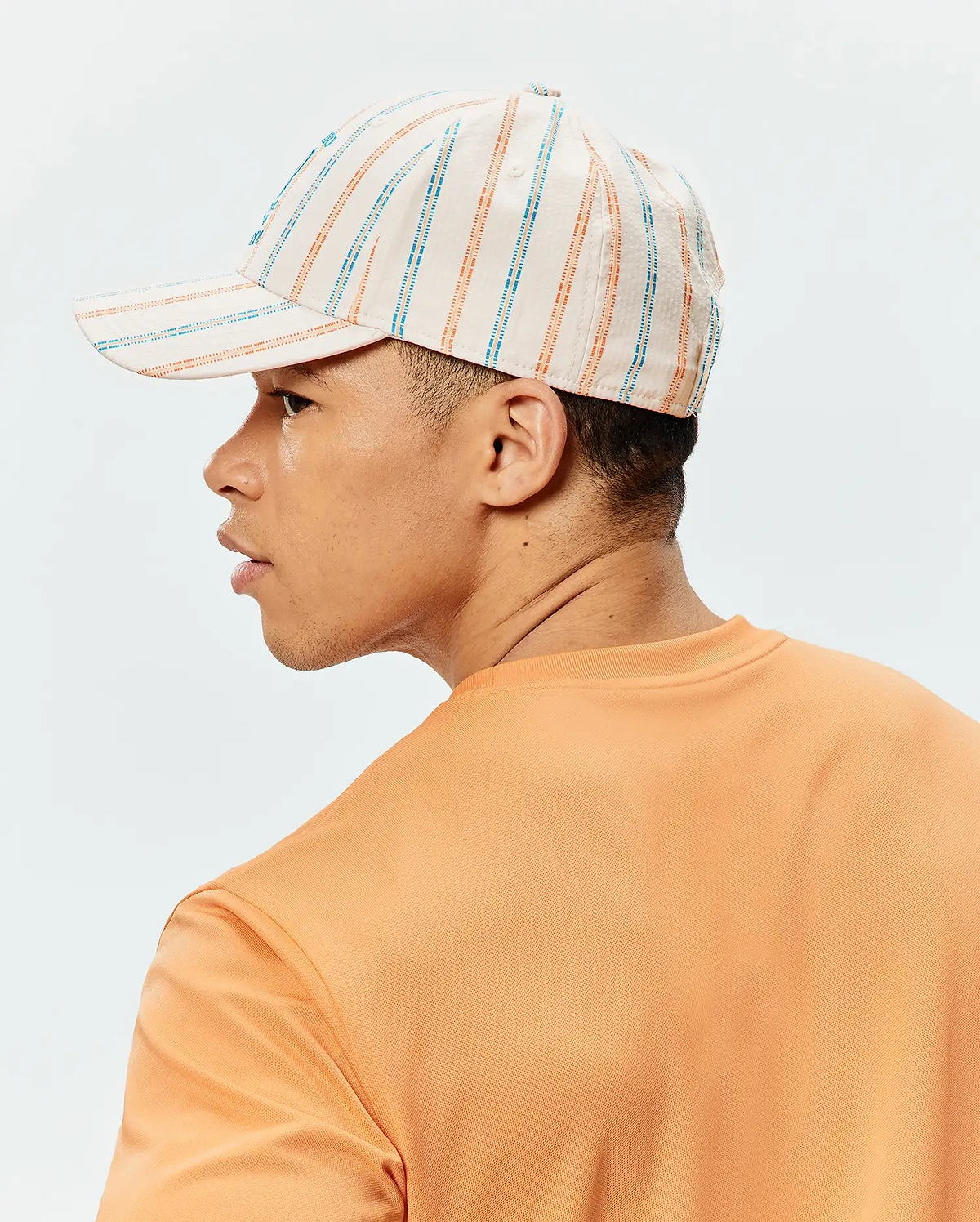 Mens Antoine Seersucker Baseball Cap in cream with orange and blue vertical stripes, paired with an orange pique knit crew neck t-shirt.