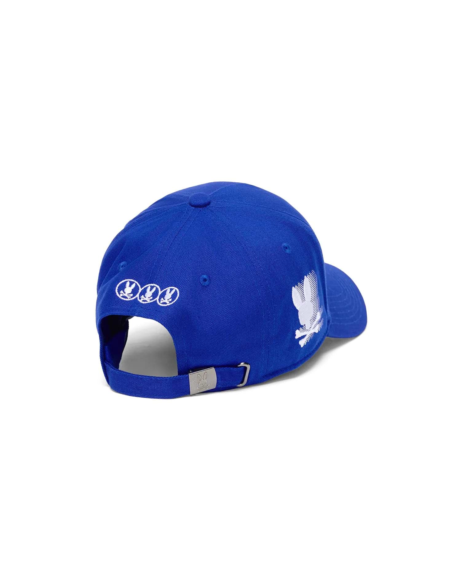 Mens Nathaniel A-Frame Trucker Cap, royal blue with a large distressed white Psycho Bunny skull logo on the right, three small white circular logos on the back, and a silver buckle with a logo.