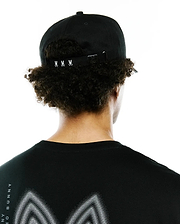 Black Mens Alex A-Frame Trucker Cap with white Psycho Bunny skull logos on the adjustable back strap, paired with a black jersey t-shirt featuring a large white dotted graphic and vertical Psycho Bunny text on the back.