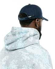 Men's Grover Baseball Cap in navy blue with light blue Psycho Bunny embroidery on the back strap and a silver bunny skull buckle, paired with a relaxed fit hoodie featuring a light blue and grey pixelated all-over print. (3)