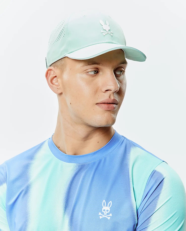 Mens Blaze Sport Cap in pale aqua with perforated sides and a white Psycho Bunny skull logo, complementing a blue, aqua, and purple tie-dye performance mesh t-shirt with a small white Psycho Bunny logo on the left chest.