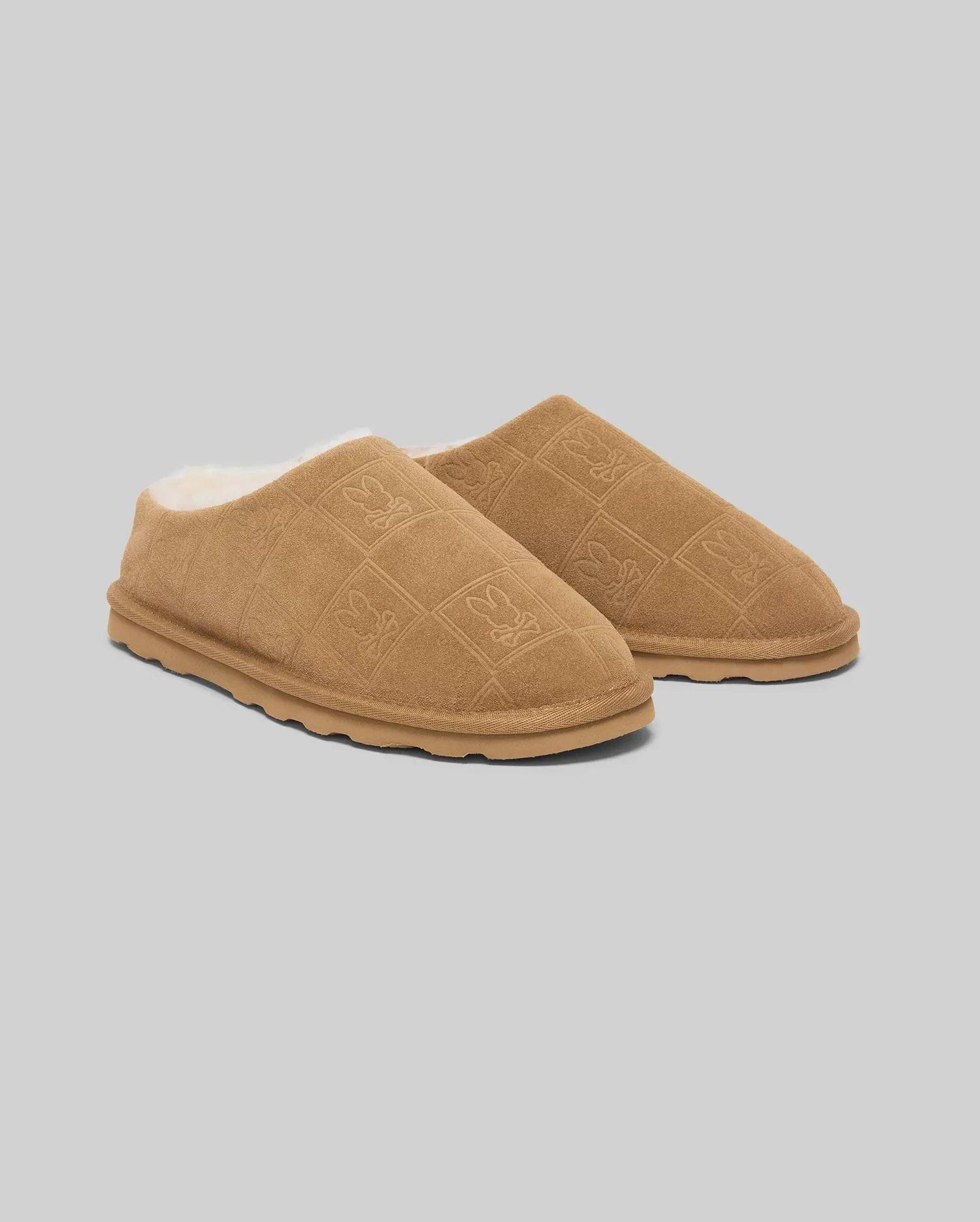 Mens Gio Suede Shearling Slippers in tan, featuring a quilted suede upper with embossed Psycho Bunny skull logos and a cozy white shearling lining.