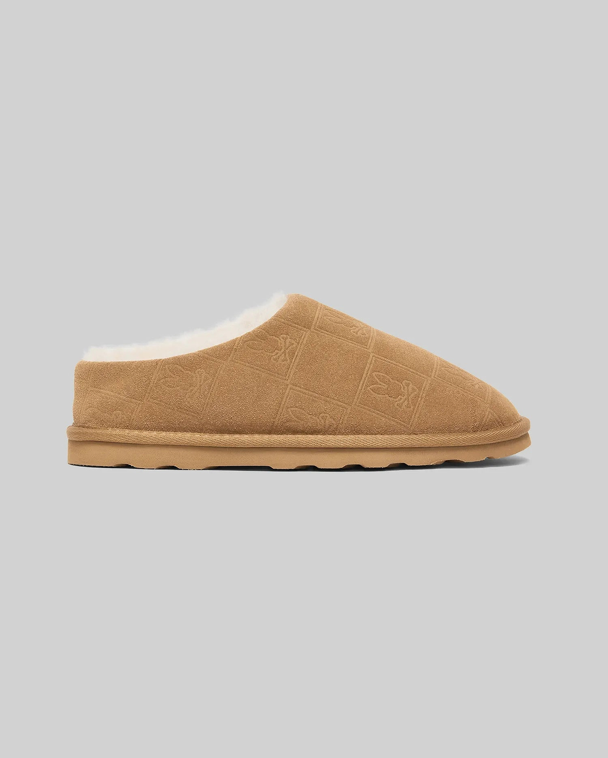 Mens Gio Suede Shearling Slippers in tan suede with plush white shearling lining, featuring an all-over debossed Psycho Bunny skull logo in a diamond grid pattern.