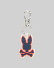 Rubber Bunny Keychain with a prominent navy Psycho Bunny skull and crossbones logo, accented by vibrant orange and pink outlines on a white rubber base, attached to a sleek silver carabiner clip.