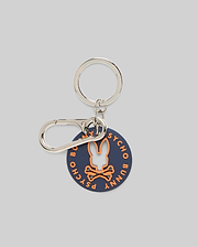 Disc Bunny Keychain featuring a navy circular disc with an orange Psycho Bunny skull logo cutout and orange brand name text, attached to a silver metal keyring and carabiner clip.