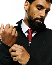 Black textured quarter-zip with embroidered Psycho Bunny skull logo on chest and branded zipper pull, worn over a white shirt and a red Mens Bunny Neat Woven Tie featuring an all-over skull pattern.