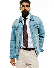 Mens Bunny Stripe Woven Tie in burgundy with white diagonal Psycho Bunny skull logos, paired with a crisp white collared shirt, light wash denim jacket featuring an orange cuff logo, and beige chinos.