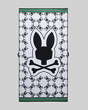 Mens All Over Bunny Towel in white terry cloth, featuring a large central black Psycho Bunny skull logo, an all-over repeating smaller black bunny skull pattern, and green and black striped borders.