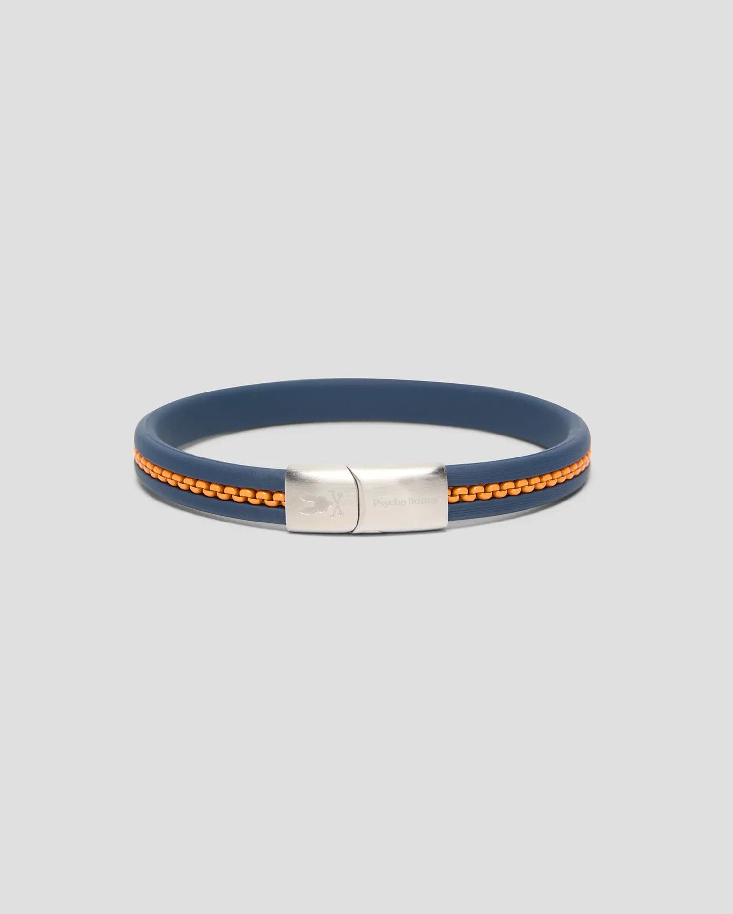 Mens Link Rubber Bracelet in navy blue rubber with an embedded orange chain detail, featuring a silver-toned metal clasp engraved with the Psycho Bunny skull logo and text.