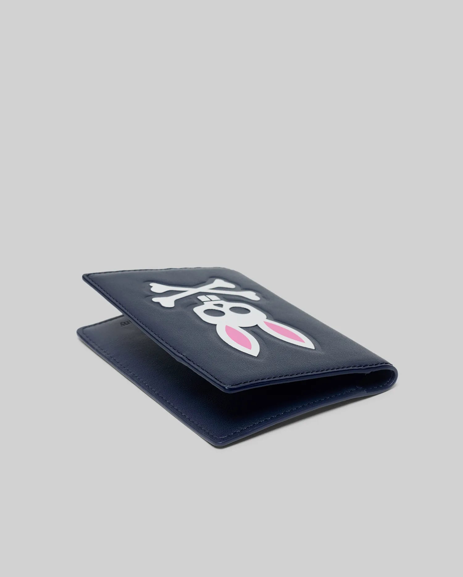 Premium navy blue Passport Holder featuring a prominent, embossed white Psycho Bunny skull logo with distinctive pink inner ears on its smooth, refined faux leather surface.