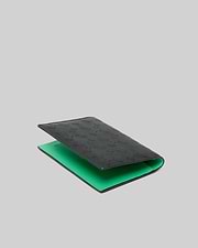 Passport Holder, black with a smooth leather-like texture, featuring an all-over embossed Psycho Bunny skull logo pattern on the exterior and a vibrant green interior. (1)