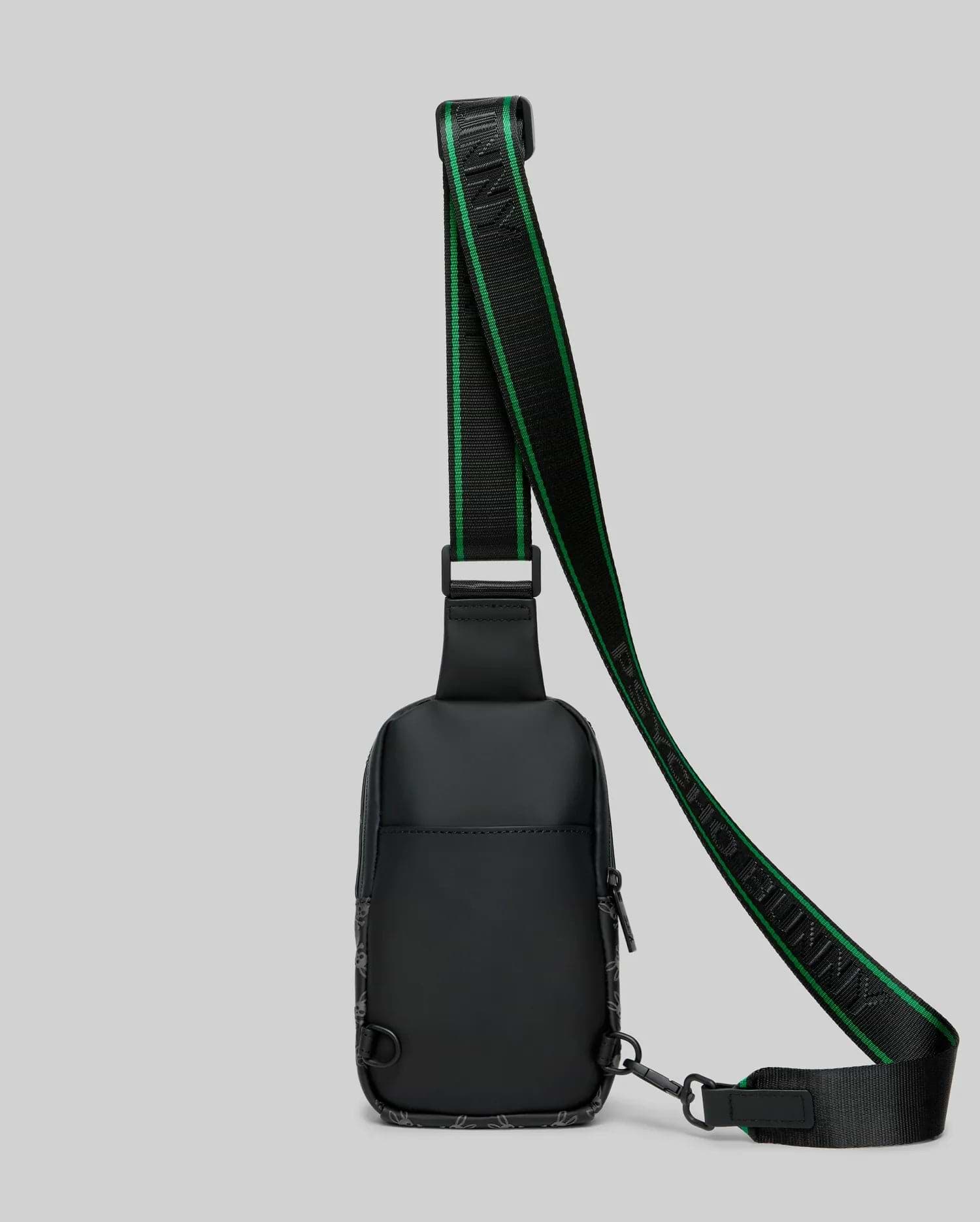 Mens Rubberized Crossbody in black, featuring a subtle all-over bunny skull pattern, a prominent green-striped strap with PSYCHO BUNNY text, and a sleek, compact design.