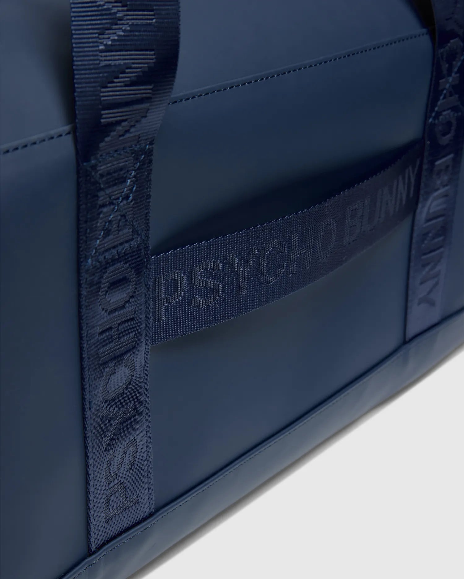 Sleek navy Classic Bunny Gym Bag with a smooth, matte texture and woven straps featuring repeated tonal Psycho Bunny logo text.