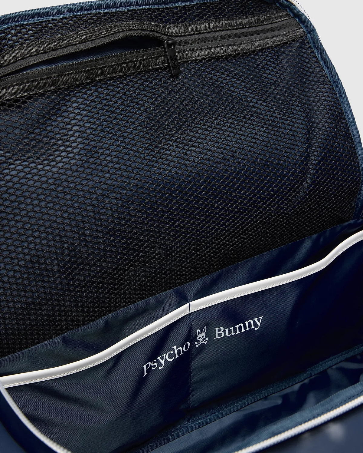 Classic Bunny Gym Bag interior featuring a navy blue lining, black mesh zippered pocket, white piping, and a prominent white Psycho Bunny skull logo print.