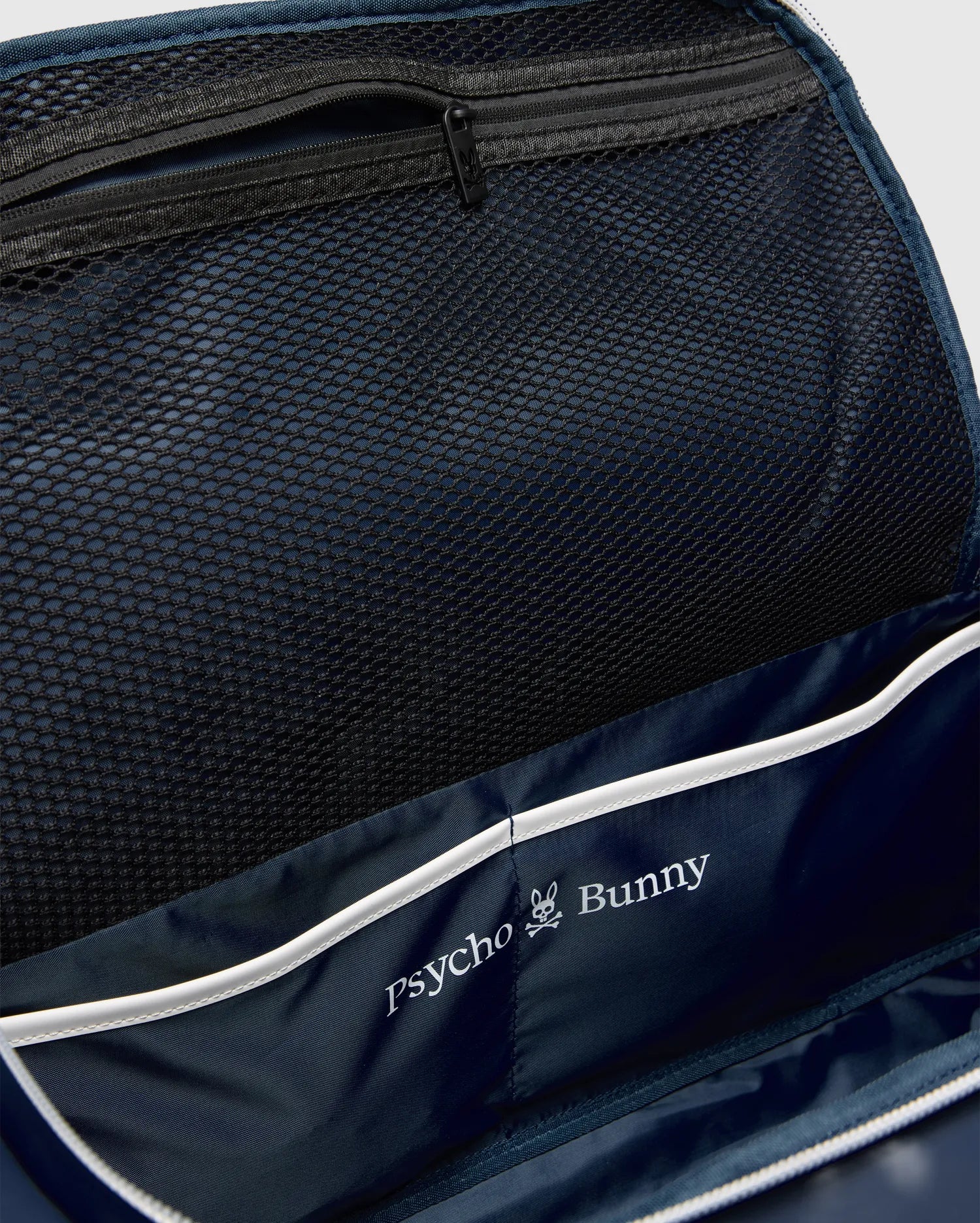 Classic Bunny Gym Bag interior featuring a navy blue lining, black mesh zippered pocket, white piping, and a prominent white Psycho Bunny skull logo print.