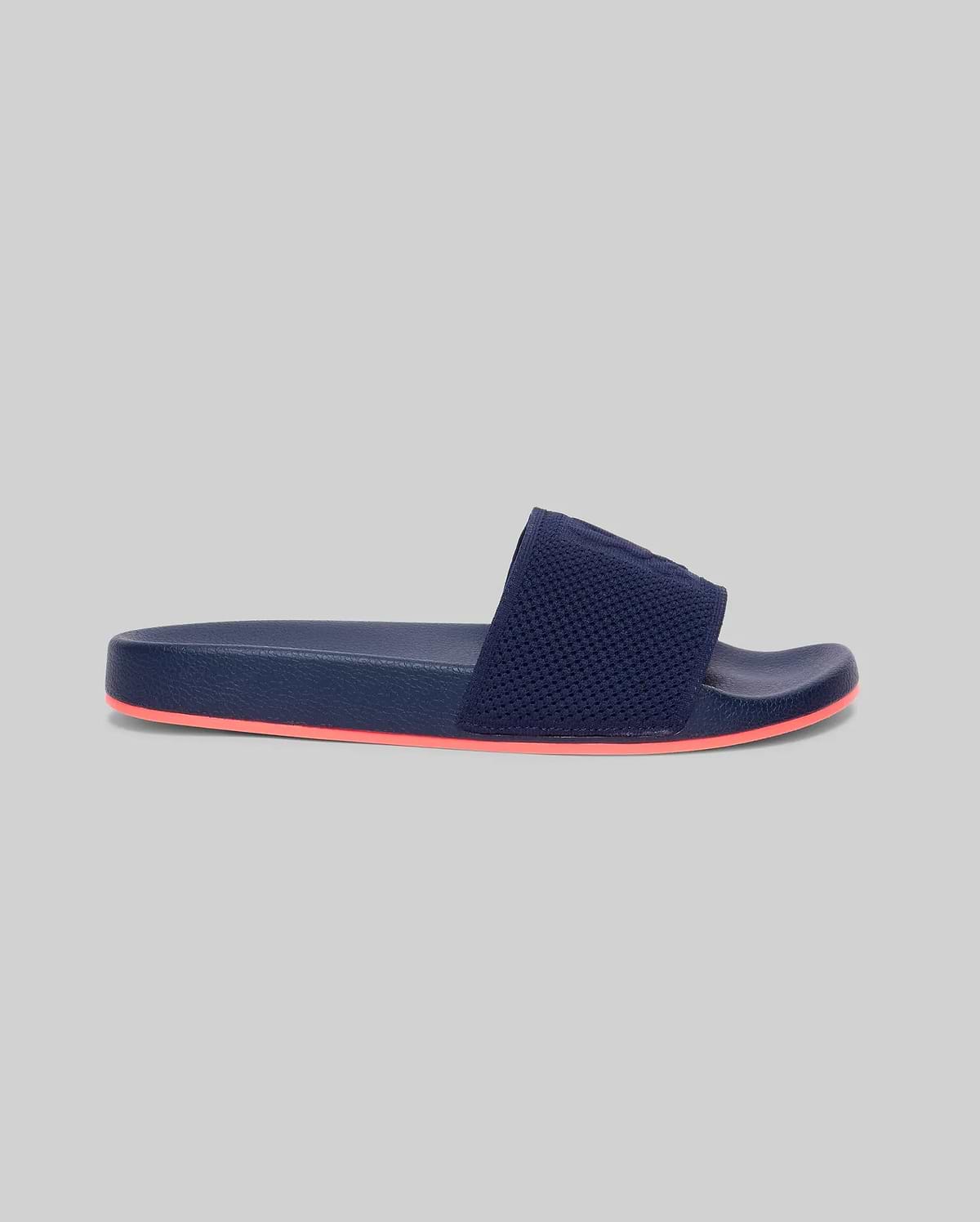 Mens Contrast Sole Knit Slides, premium Psycho Bunny footwear, in deep navy with a textured knit strap featuring subtle branding and a vibrant coral contrast sole for refined streetwear style.