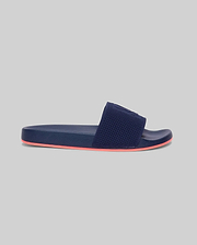 Mens Contrast Sole Knit Slides, premium Psycho Bunny footwear, in deep navy with a textured knit strap featuring subtle branding and a vibrant coral contrast sole for refined streetwear style.