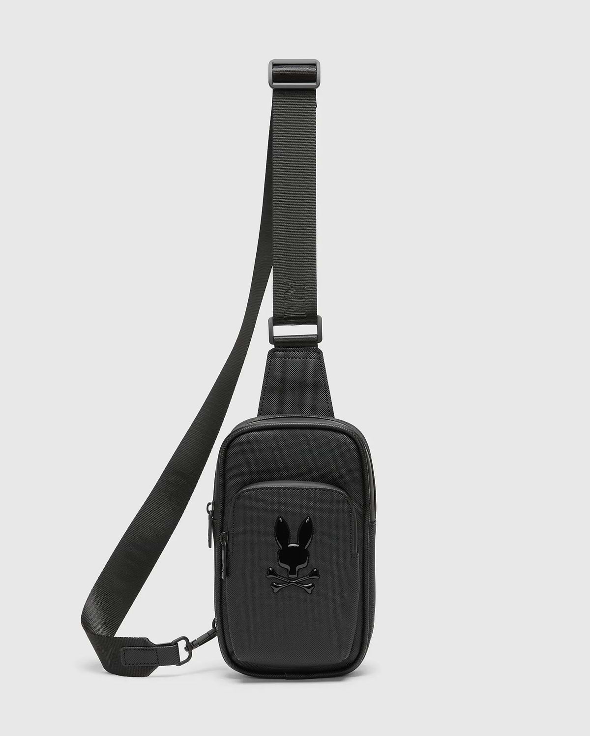 Black Crossbody Bag crafted from a refined Saffiano-style textured material, featuring a prominent glossy black Psycho Bunny skull logo on the front pocket and a durable adjustable strap. (1)