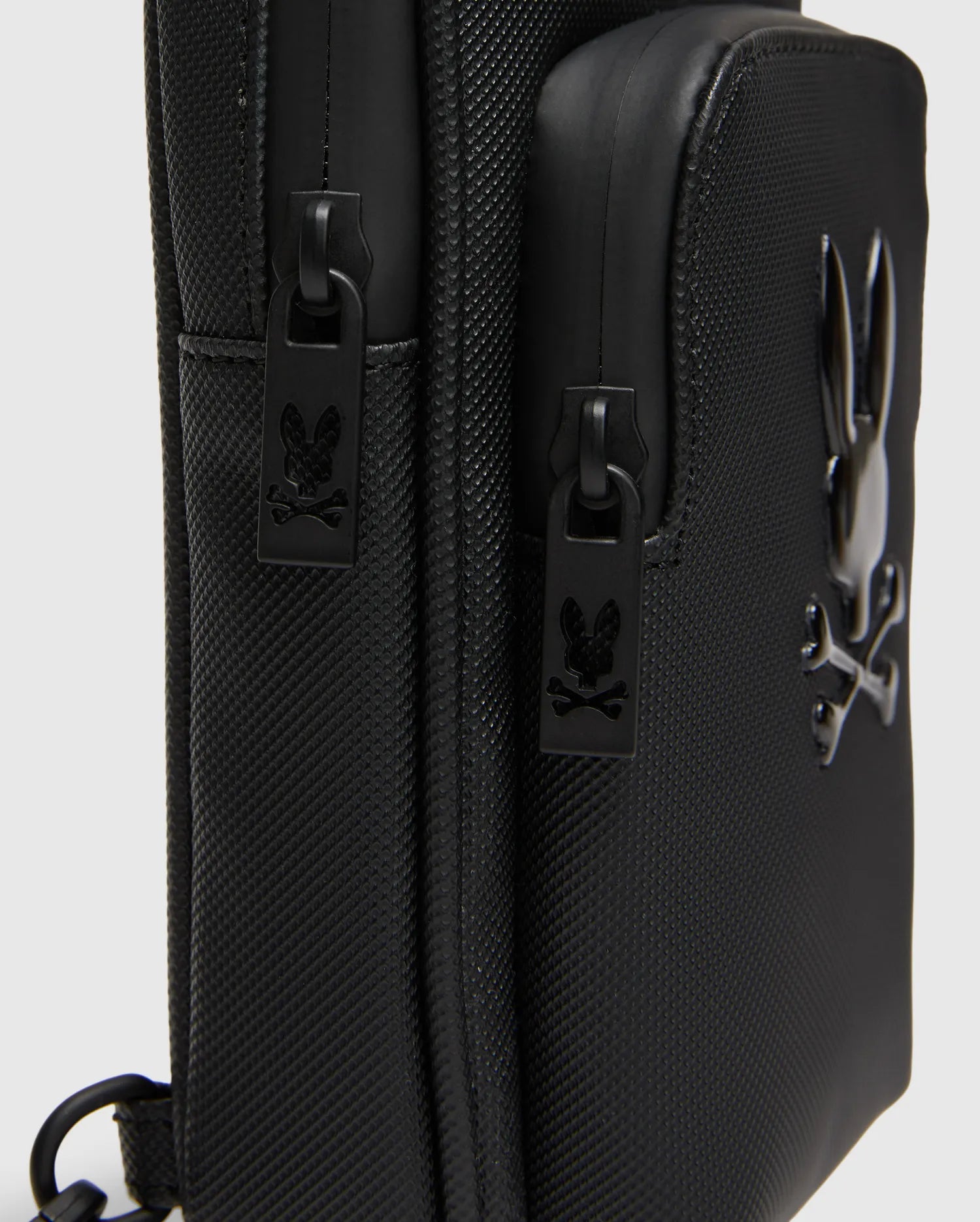 Black Crossbody Bag with durable textured fabric, featuring a prominent glossy raised Psycho Bunny skull logo and custom black zipper pulls with the logo. (3)