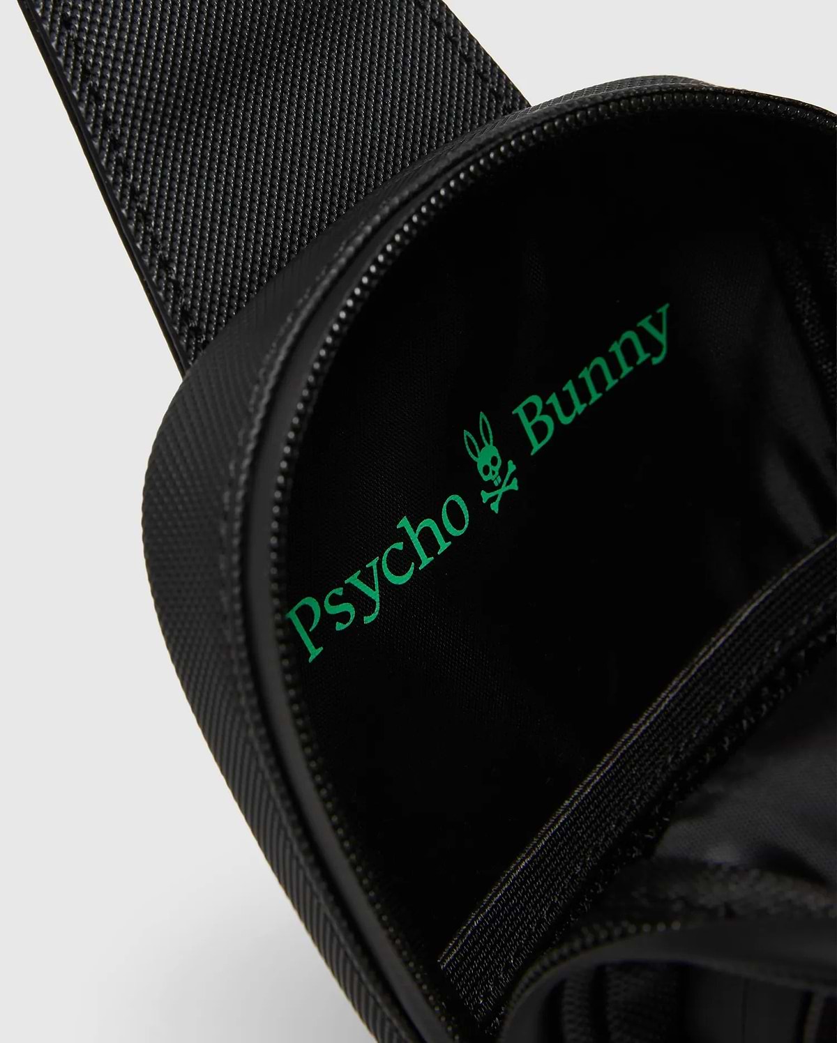 Black textured Crossbody Bag with a bright green Psycho Bunny logo and text printed large inside the main compartment, featuring a durable zipper closure. (2)