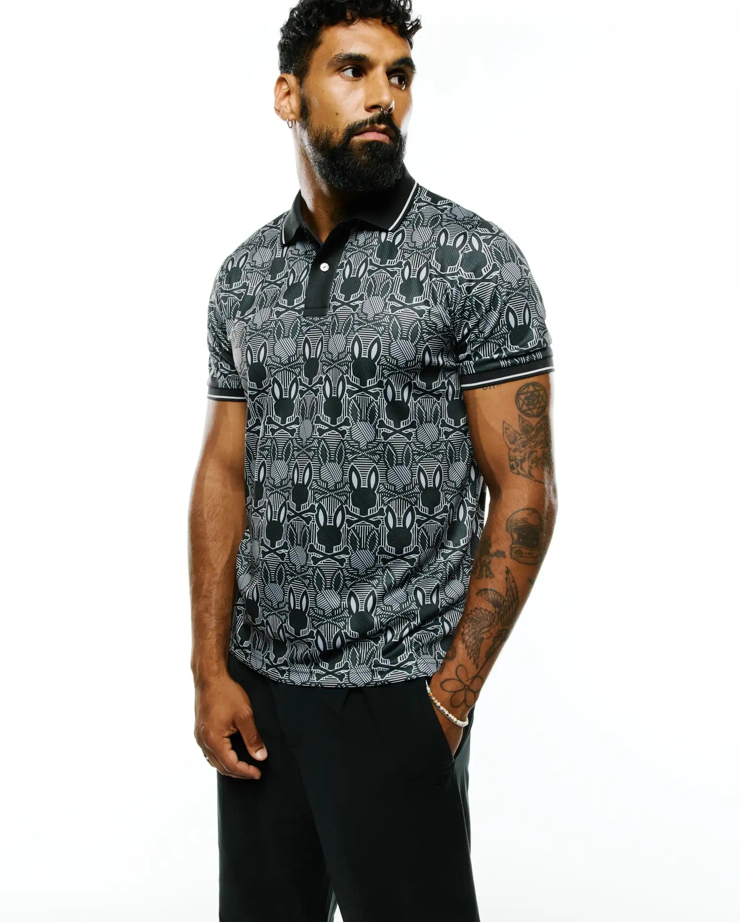 Mens Reeves All Over Bunny Sport Polo, a black and white all-over bunny skull pattern polo shirt with a classic fit, smooth performance fabric, black collar, and white striped cuffs.