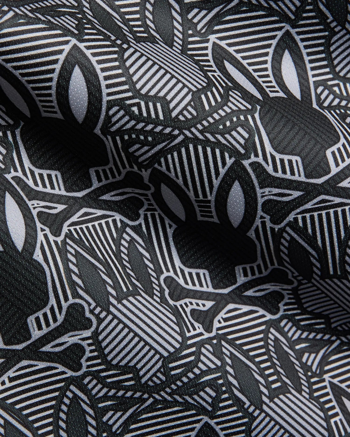 Mens Reeves All Over Bunny Sport Polo in black, white, and grey, featuring an all-over Psycho Bunny skull and crossbones print on a geometric striped performance fabric.