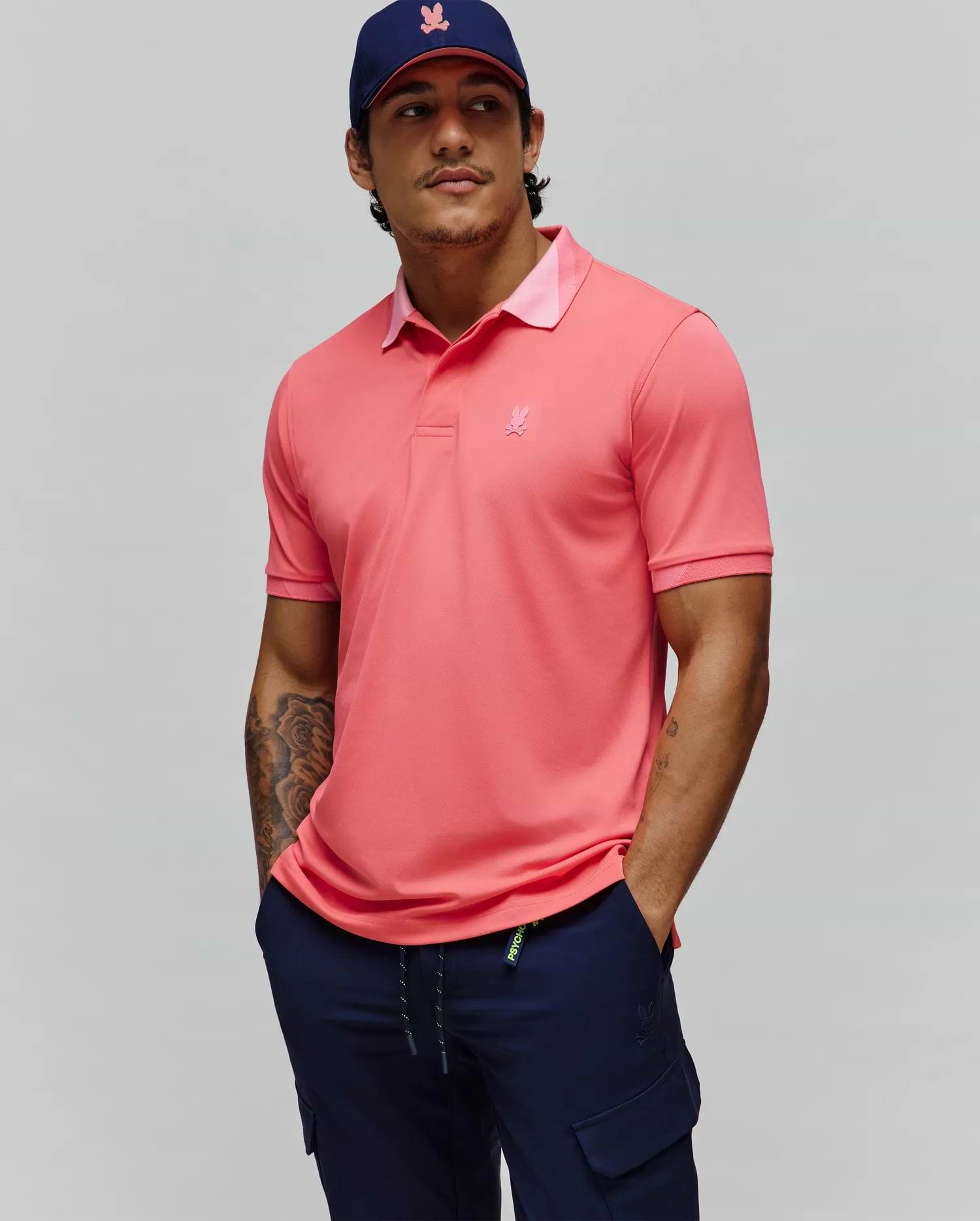 Mens Onyx Sport Polo, a vibrant coral performance polo with a classic fit, features a lighter pink collar underside, ribbed cuffs, and a small tonal embroidered Psycho Bunny skull logo on the left chest.