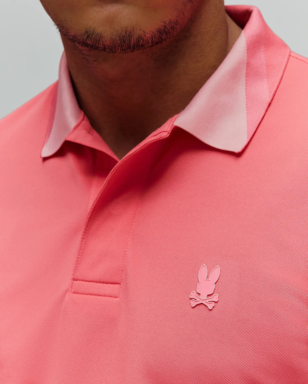 Mens Onyx Sport Polo in vibrant coral pique knit, classic fit, featuring a lighter pink collar accent and a small, embroidered pink Psycho Bunny skull logo on the left chest.