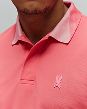 Mens Onyx Sport Polo in vibrant coral pique knit, classic fit, featuring a lighter pink collar accent and a small, embroidered pink Psycho Bunny skull logo on the left chest.