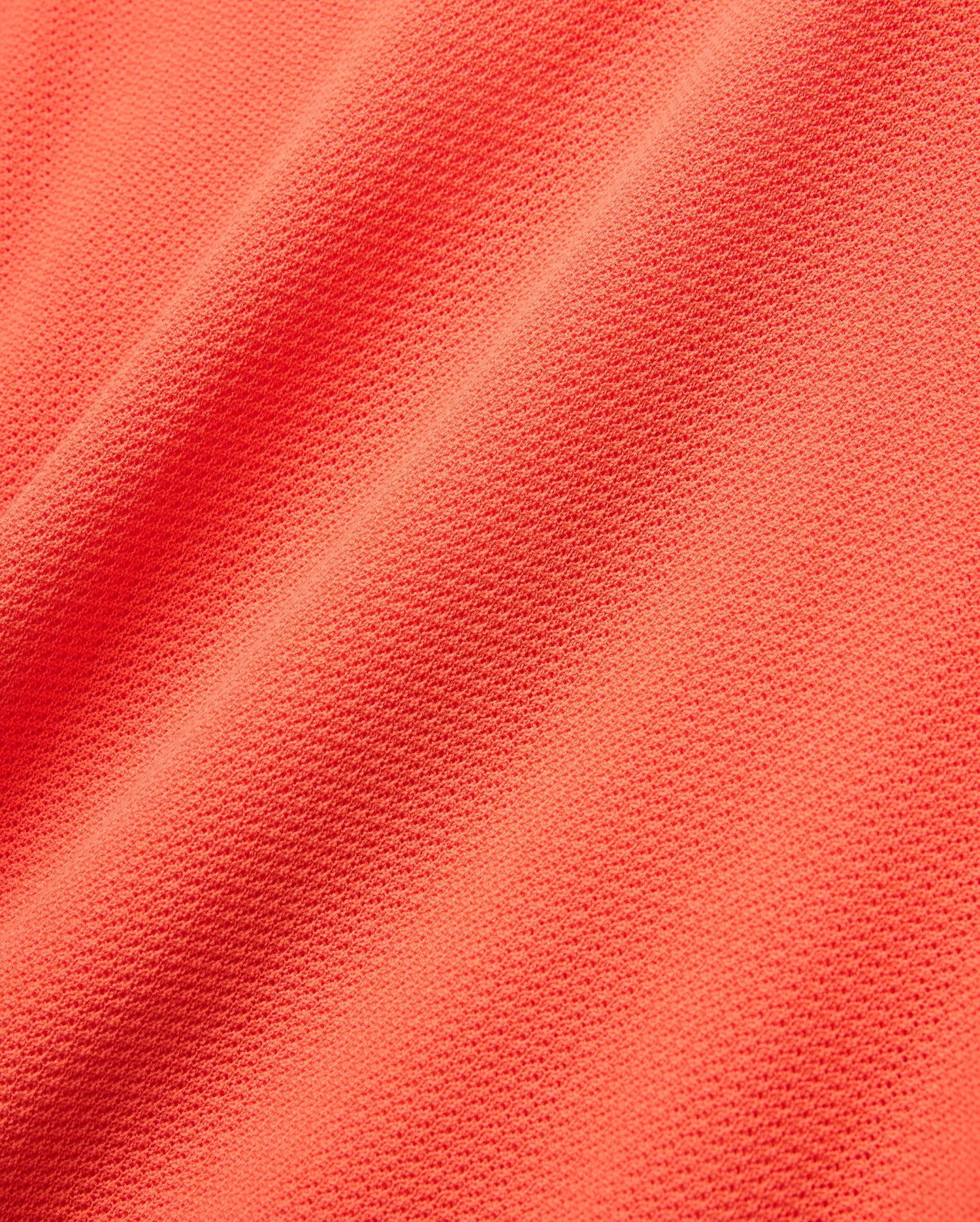 Mens Innis Polo in vibrant coral orange pique knit fabric, showcasing its signature textured, breathable weave with subtle diagonal folds, ideal for premium Psycho Bunny refined streetwear. (5)