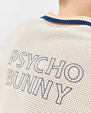 Mens Theros Knit Polo in cream with a textured open knit, featuring a navy and orange striped collar and large embroidered PSYCHO BUNNY text in navy and light beige on the upper back.