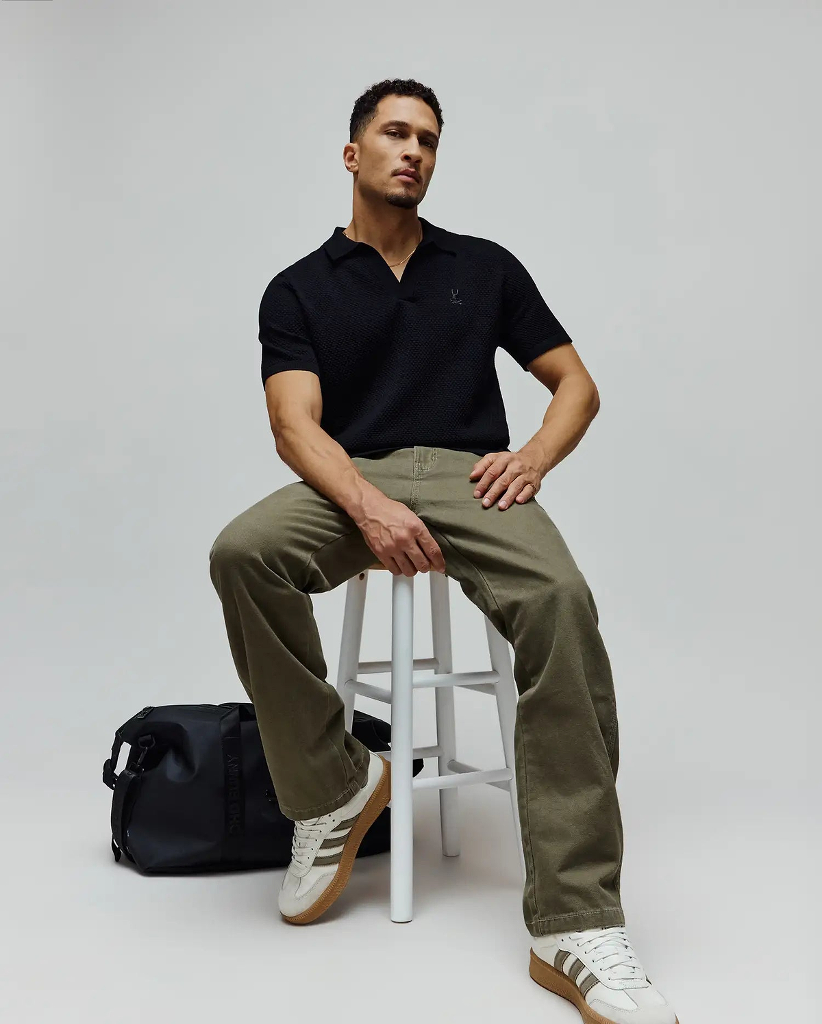 Mens Devon Knit Polo in black, featuring a refined textured knit fabric, an open collar, and a small embroidered Psycho Bunny skull logo on the left chest for a classic fit.