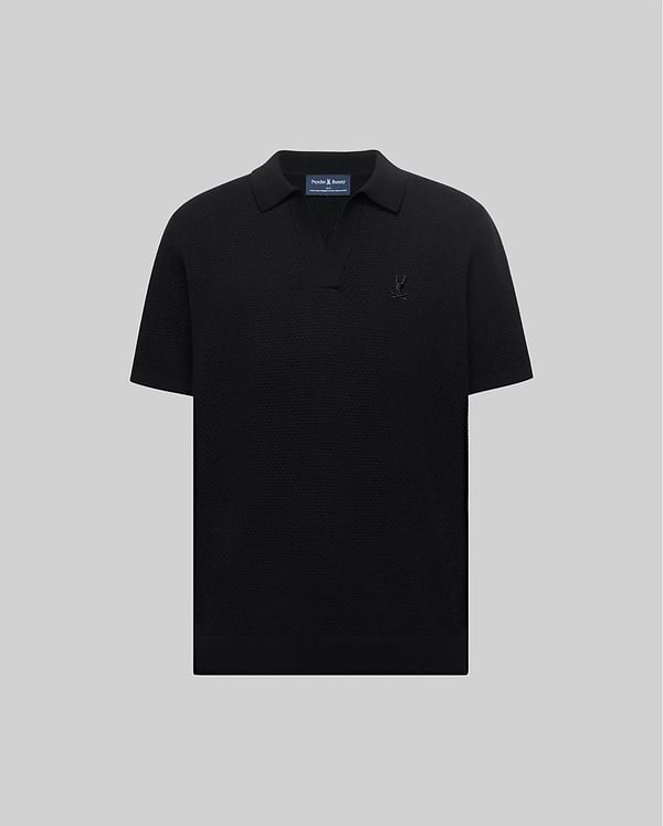Mens Devon Knit Polo in black, featuring a subtle textured knit, classic fit, V-neck placket, and a tonal embroidered Psycho Bunny skull logo on the left chest.