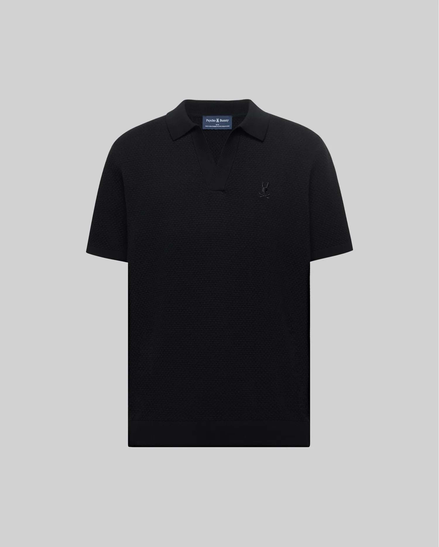 Mens Devon Knit Polo in black, featuring a subtle textured knit, classic fit, V-neck placket, and a tonal embroidered Psycho Bunny skull logo on the left chest.