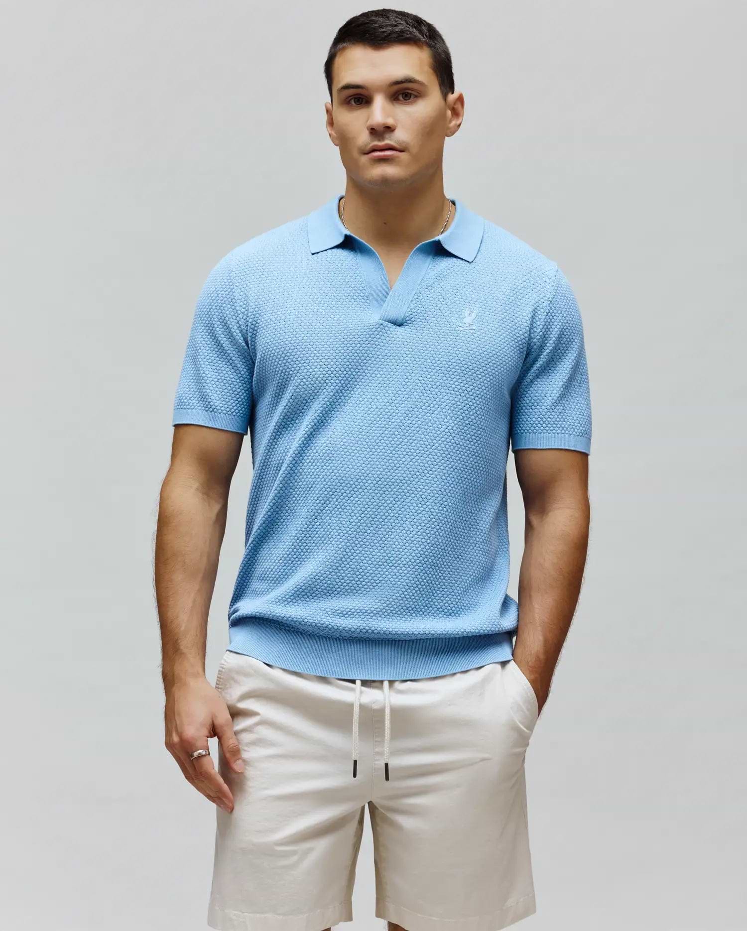 Mens Devon Knit Polo, sky blue textured knit with an open collar, classic fit, and a small embroidered white Psycho Bunny skull logo on the left chest, featuring ribbed cuffs and hem.