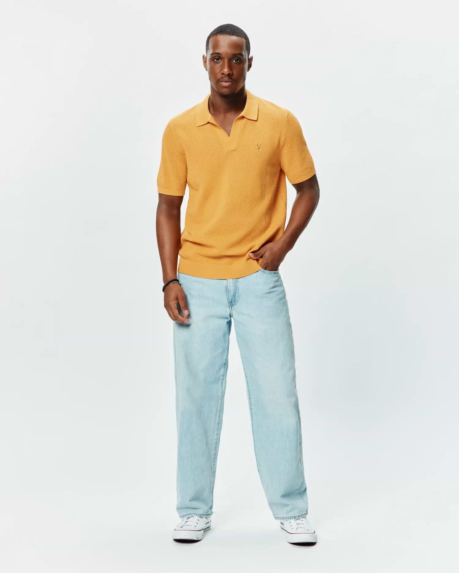 Mens Devon Knit Polo in golden yellow, featuring a textured knit fabric, classic fit, open collar, ribbed cuffs and hem, with a small embroidered Psycho Bunny skull logo on the left chest.