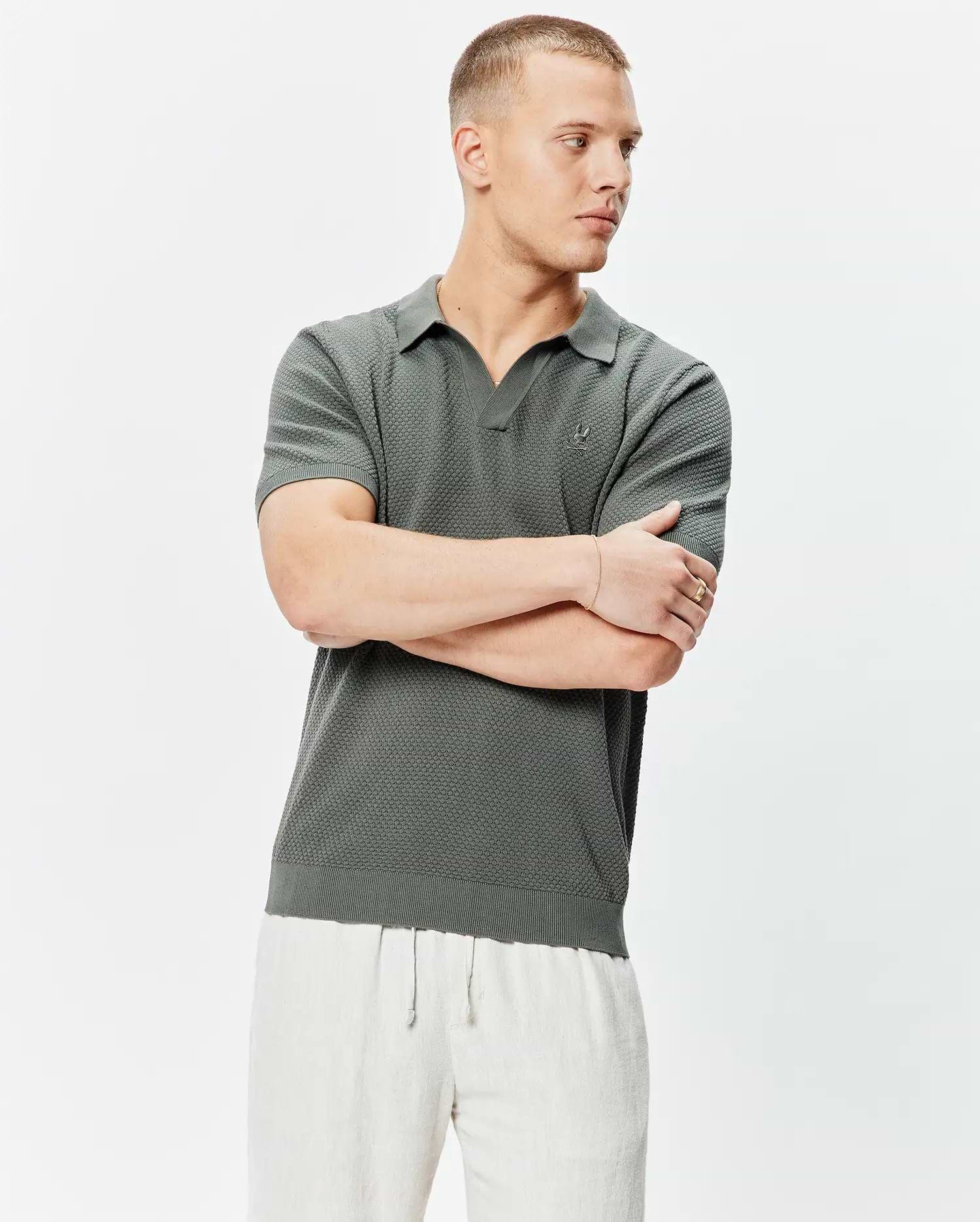 Mens Devon Knit Polo in deep olive, featuring a textured knit fabric, open collar, ribbed cuffs and hem, with a small embroidered Psycho Bunny skull logo on the left chest.