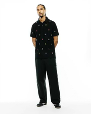Mens Colin All-Over Pique Polo, a black pique polo shirt with a classic fit, featuring an all-over embroidered pattern of small, colorful Psycho Bunny skull logos and blue wave motifs.