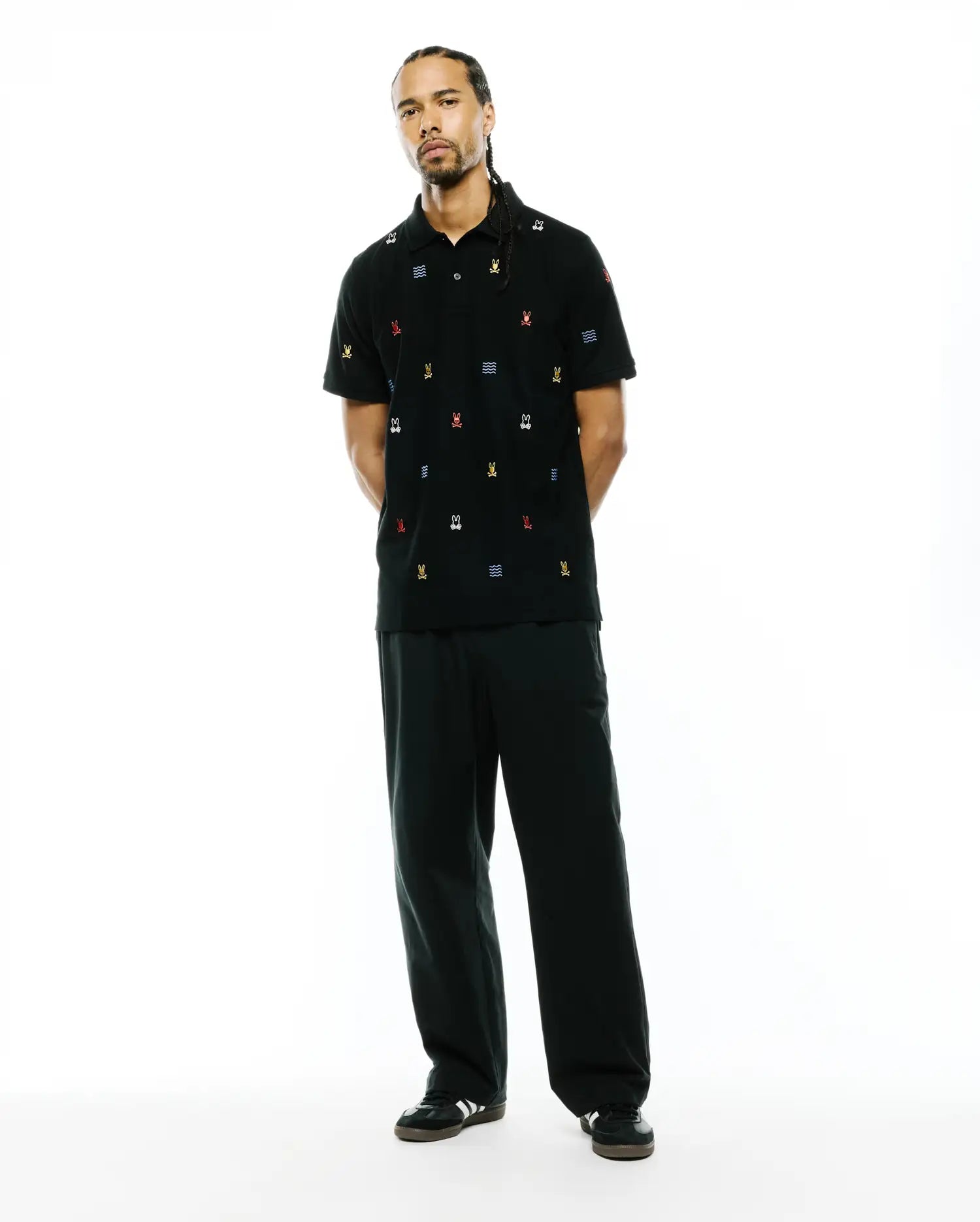 Mens Colin All-Over Pique Polo, a black pique polo shirt with a classic fit, featuring an all-over embroidered pattern of small, colorful Psycho Bunny skull logos and blue wave motifs.