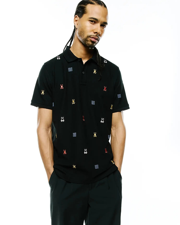 Mens Colin All-Over Pique Polo in black, featuring a classic fit and pique texture, adorned with an all-over embroidered pattern of multi-colored Psycho Bunny skull logos and blue wave graphics.