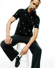 Mens Colin All-Over Pique Polo in black, featuring a classic fit and an all-over embroidered pattern of small multicolor Psycho Bunny skull logos and blue wave graphics.