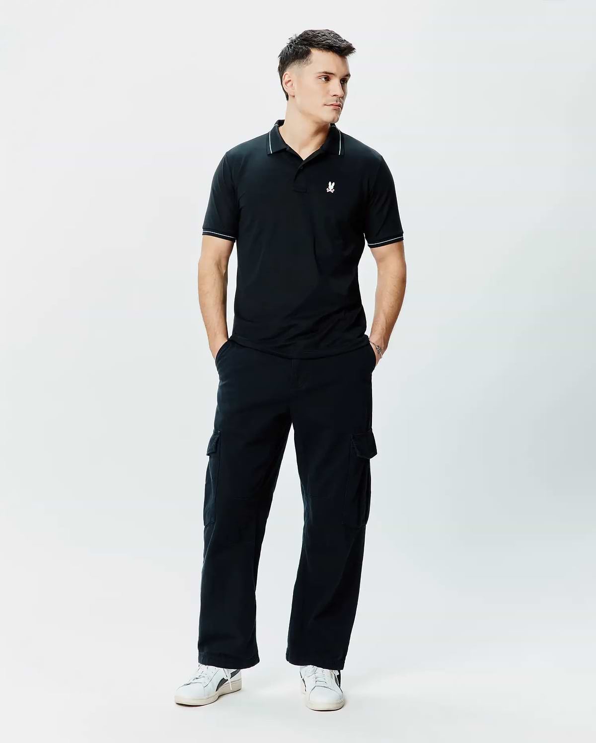 Mens Edwin Sport Polo, black pique knit polo shirt with a classic fit, featuring white piping on the collar and sleeve cuffs, and a small white embroidered Psycho Bunny skull logo on the left chest.