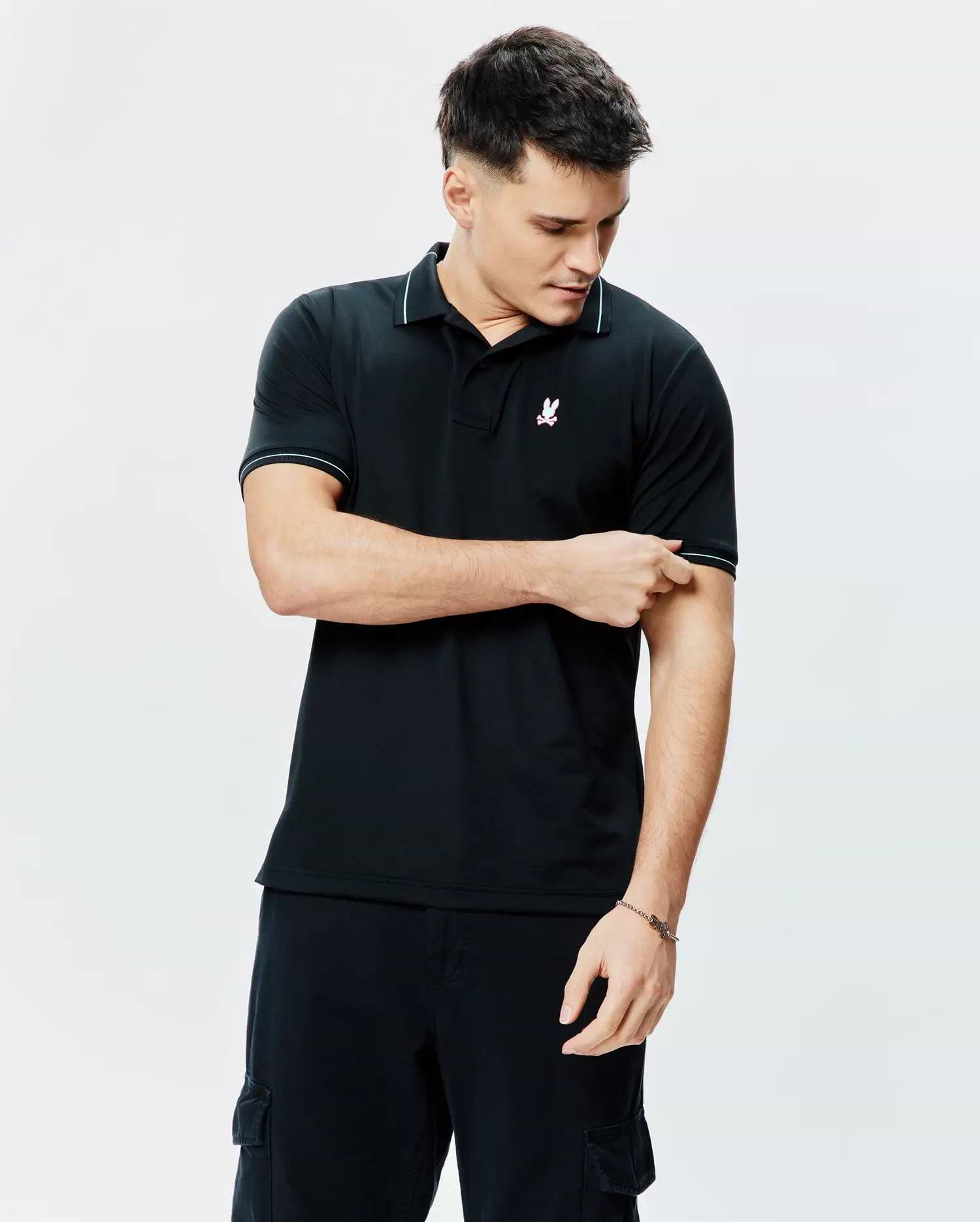 Mens Edwin Sport Polo, a classic fit black pique knit polo shirt with white tipping on the collar and cuffs, featuring a small embroidered pink, white, and light blue Psycho Bunny skull logo on the left chest.
