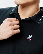 Mens Edwin Sport Polo, black pique knit with a classic fit, featuring a light blue collar stripe and an embroidered mint green and pink Psycho Bunny skull logo on the left chest.