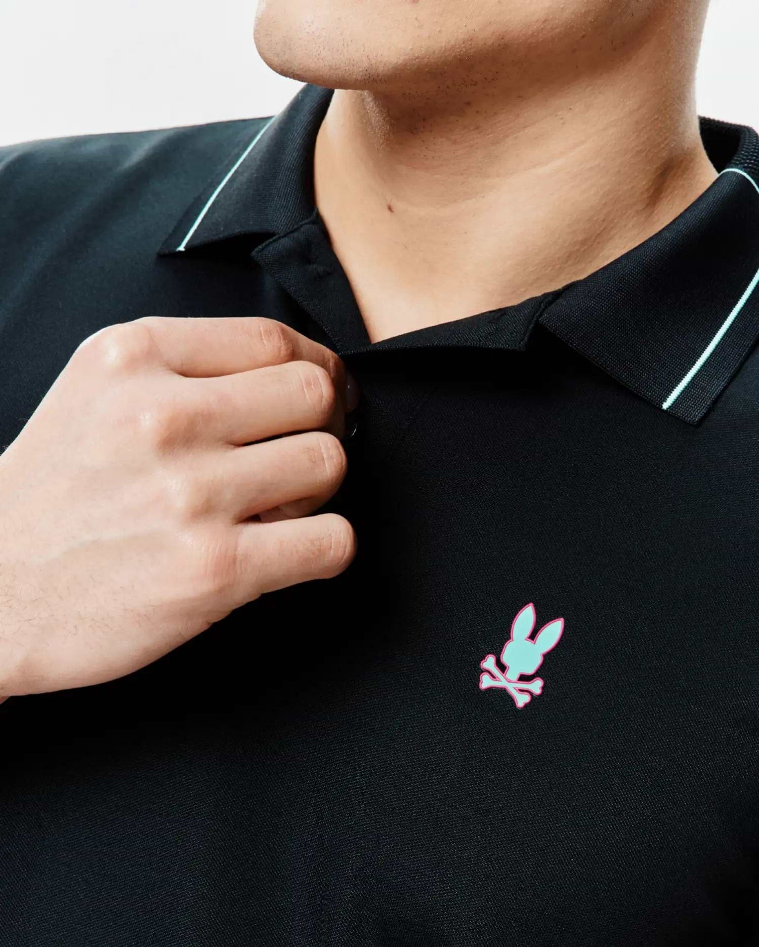 Mens Edwin Sport Polo, black pique knit with a classic fit, featuring a light blue collar stripe and an embroidered mint green and pink Psycho Bunny skull logo on the left chest.