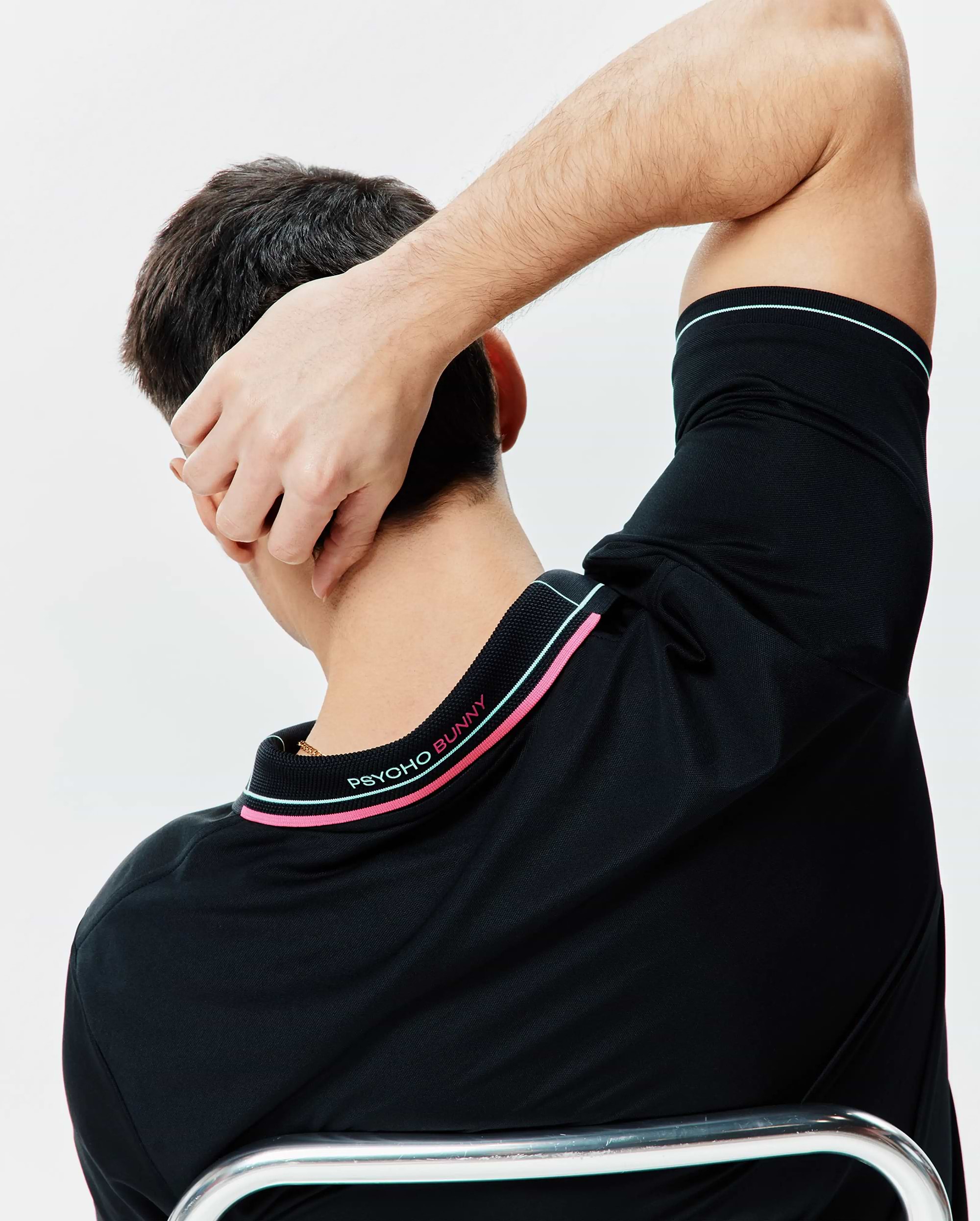 Black Mens Edwin Sport Polo, classic fit performance jersey, with pink and light blue striped ribbed collar and sleeve cuffs, featuring embroidered PSYCHO BUNNY text on the back collar.