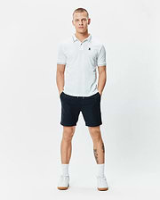 Mens Edwin Sport Polo, a classic fit white pique polo with navy tipping on the collar and cuffs, featuring a small embroidered teal Psycho Bunny skull logo on the left chest.