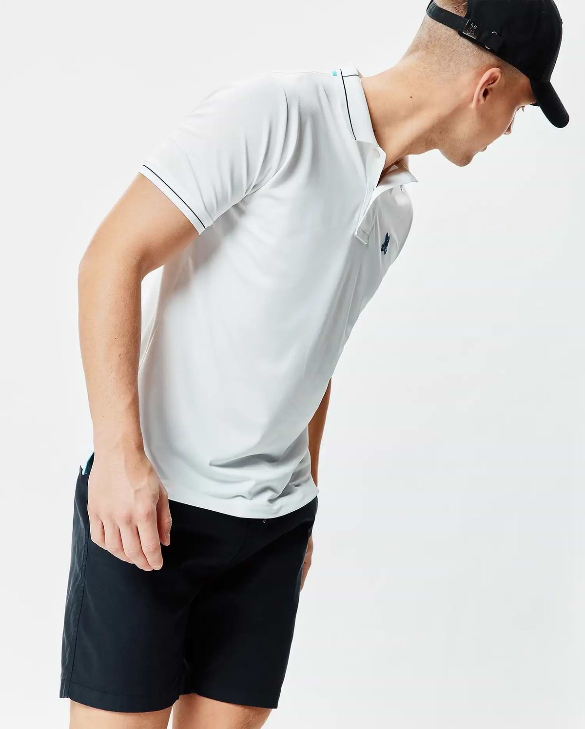 Mens Edwin Sport Polo, a white classic fit performance knit polo with black tipping on the collar and sleeves, a light blue inner collar stripe, and a small embroidered teal Psycho Bunny skull logo on the left chest.