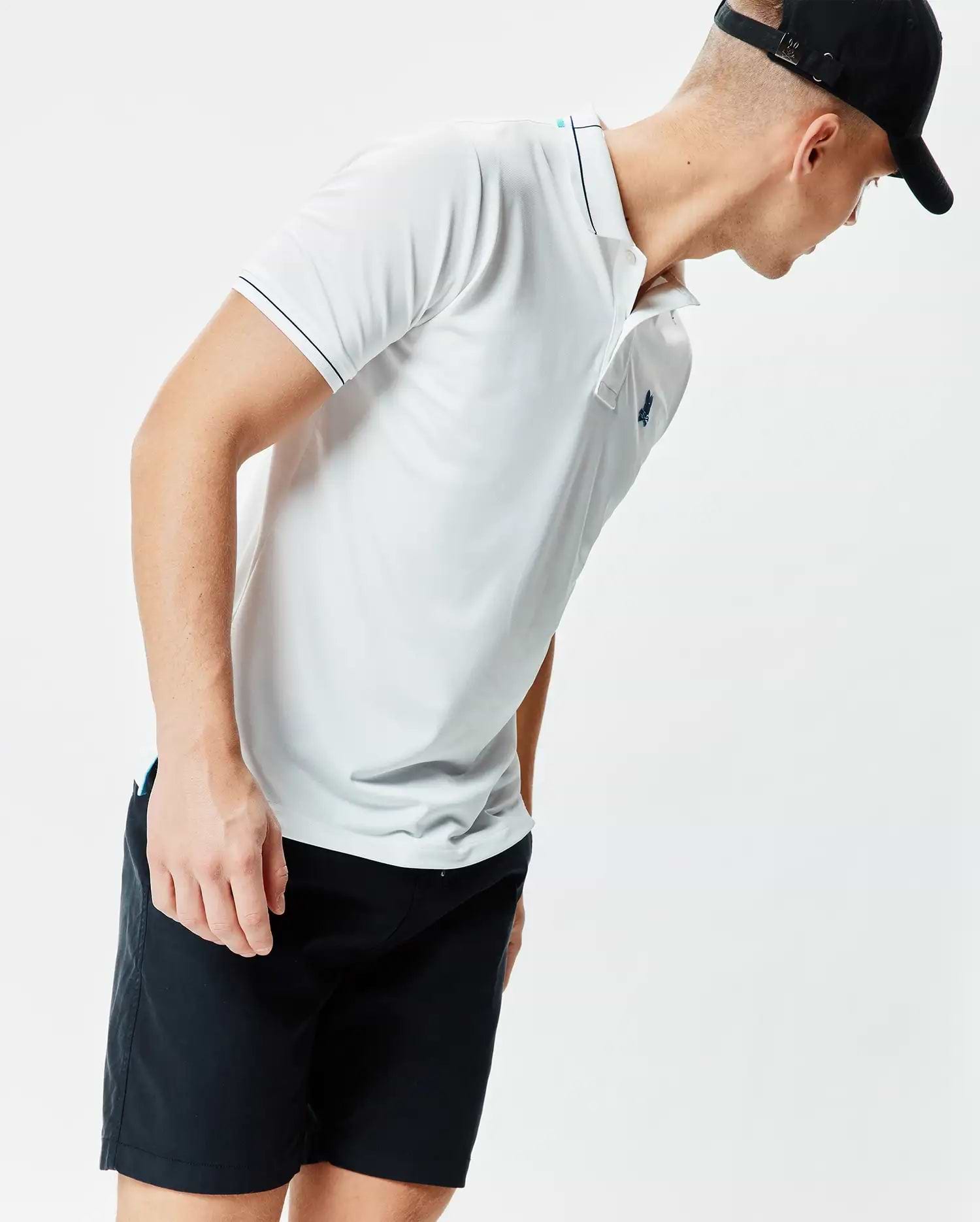 Mens Edwin Sport Polo, a white classic fit performance knit polo with black tipping on the collar and sleeves, a light blue inner collar stripe, and a small embroidered teal Psycho Bunny skull logo on the left chest.