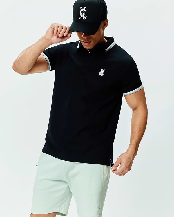 Mens Holden Pique Polo, a black classic fit pique knit polo with white and grey tipping on the collar and sleeve cuffs, featuring a small embroidered Psycho Bunny skull logo on the left chest.